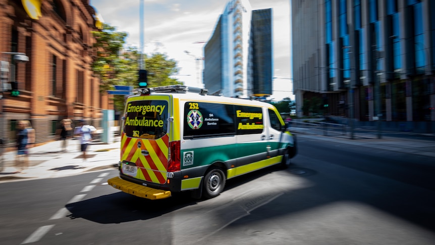 An ambulance driving on a city street with buildings on either side