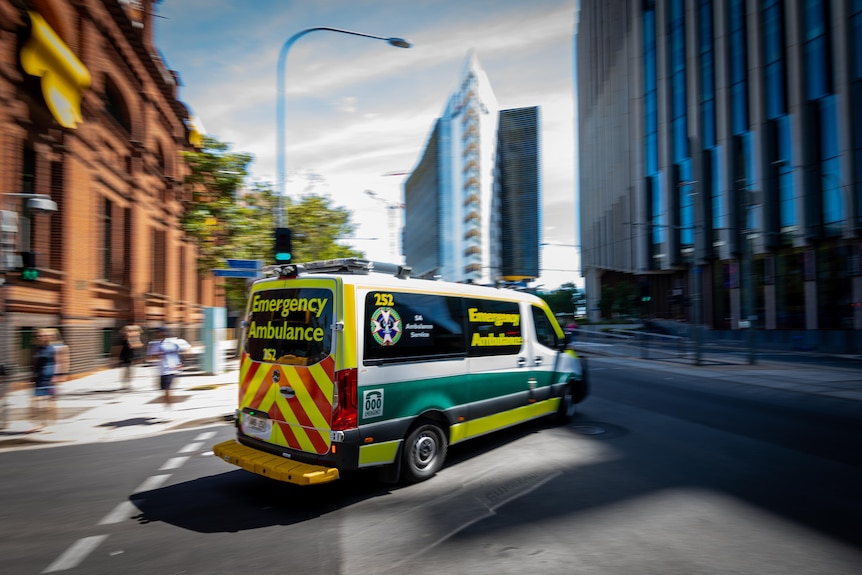 An ambulance driving on a city street with buildings on either side