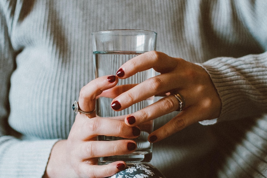 A woman holds a glass of water on her lap, attempting to drink the recommended amount over the day.