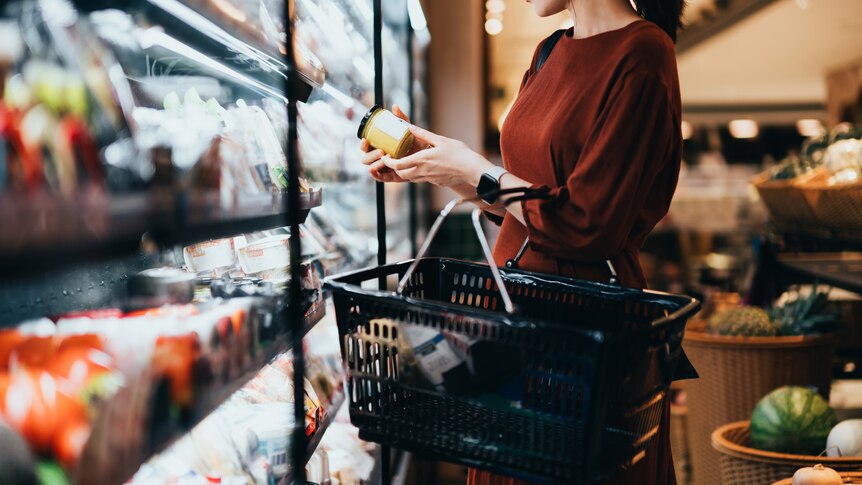 young woman with shopping basket reading nutrition label in supermarket