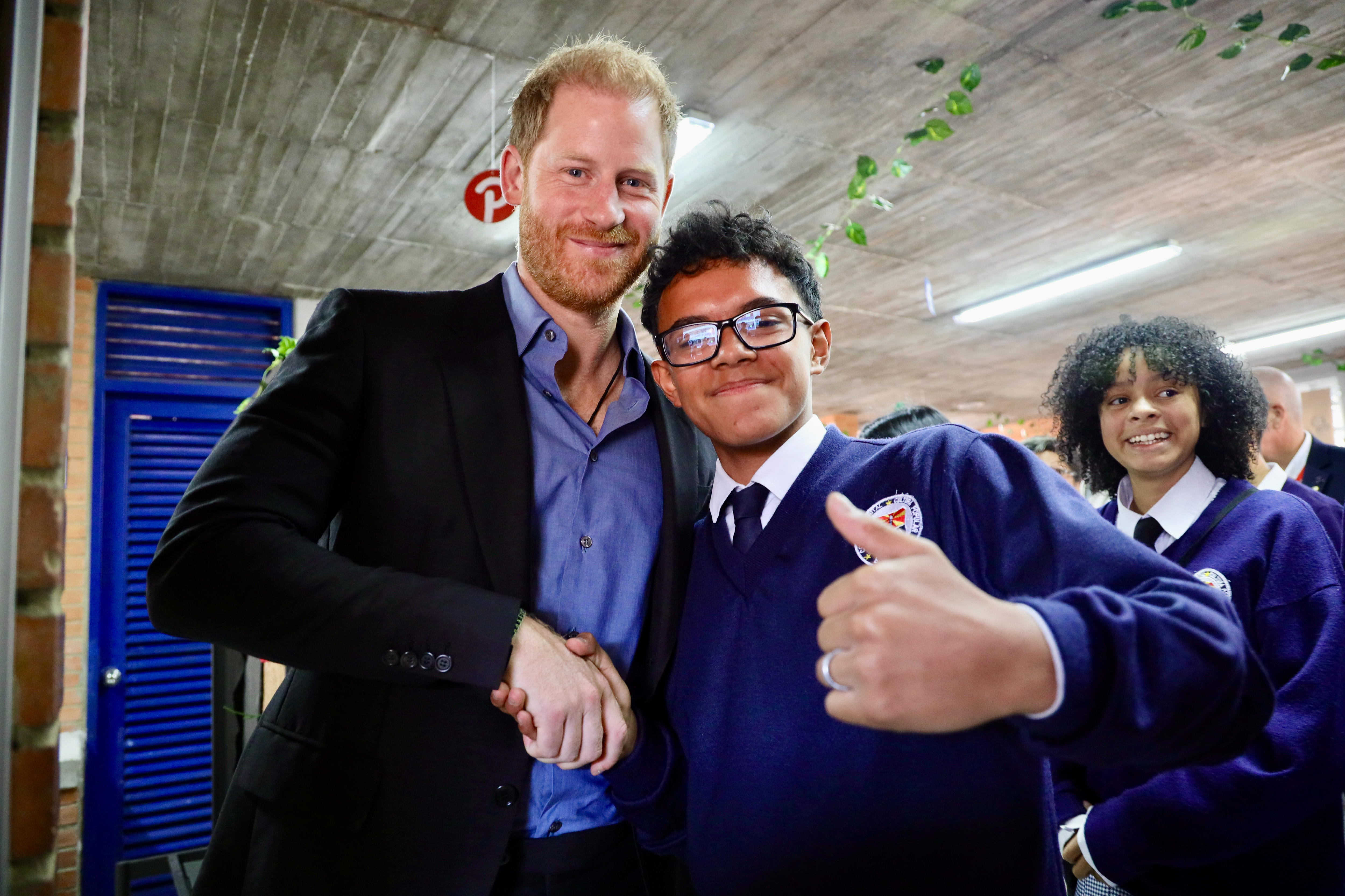 Prince Harry shakes the hand of a schoolboy, who is giving the thumbs up to the camera.
