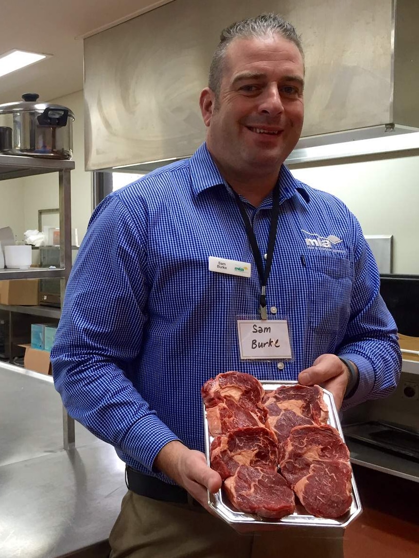 MLA's corporate chef, Sam Burke holding a tray of steaks in an industrial kitchen.
