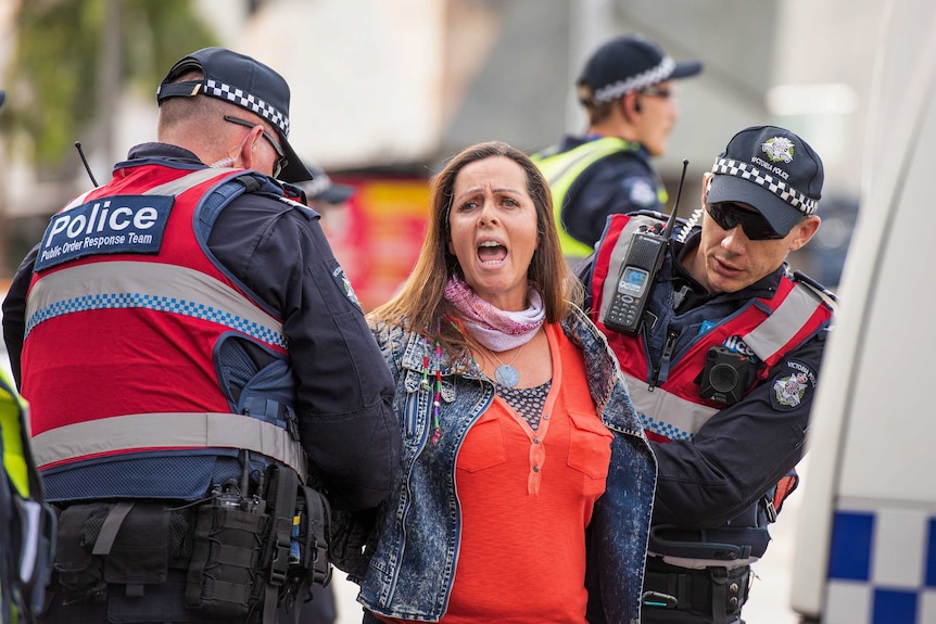 Police in vests hold down the arms of a woman in the CBD.