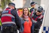 Police in vests hold down the arms of a woman in the Melbourne CBD.