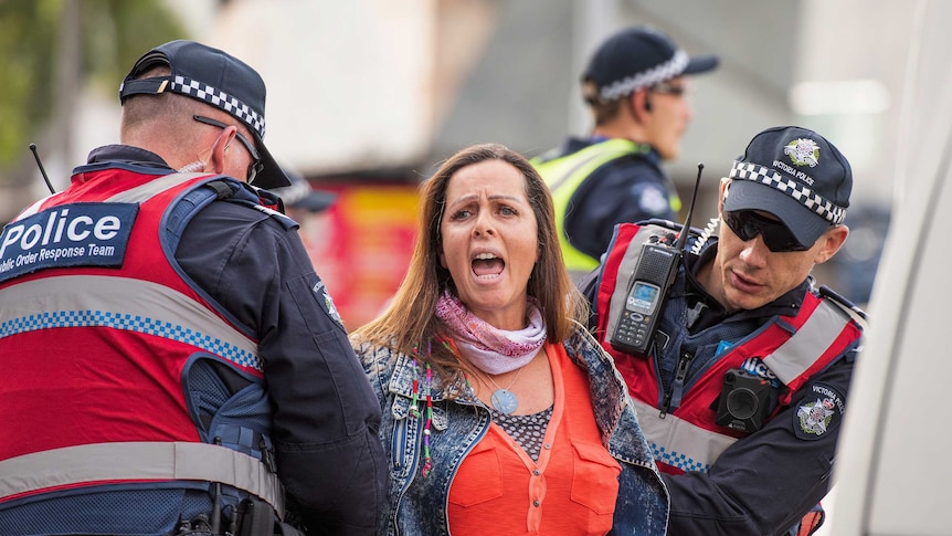 Police in vests hold down the arms of a woman in the CBD.