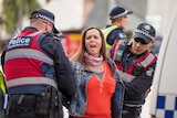 Police in vests hold down the arms of a woman in the Melbourne CBD.