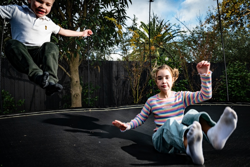 A young white boy and girl bouncing on a backyard trampoline