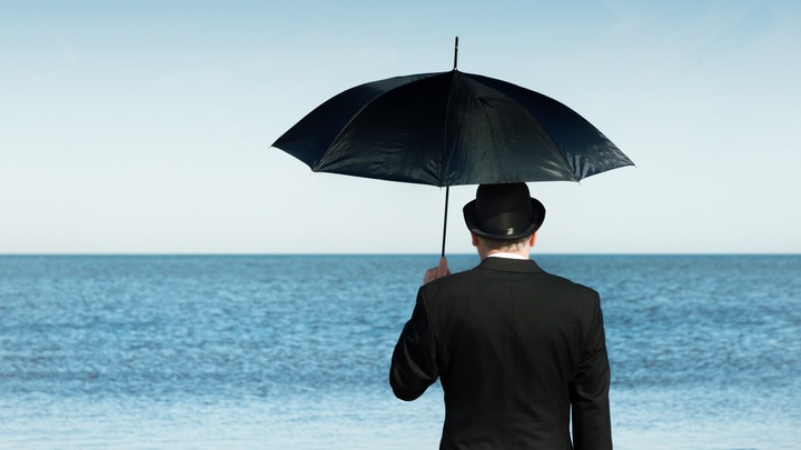 bowler-hatted businessman with umbrella looks out to the sea