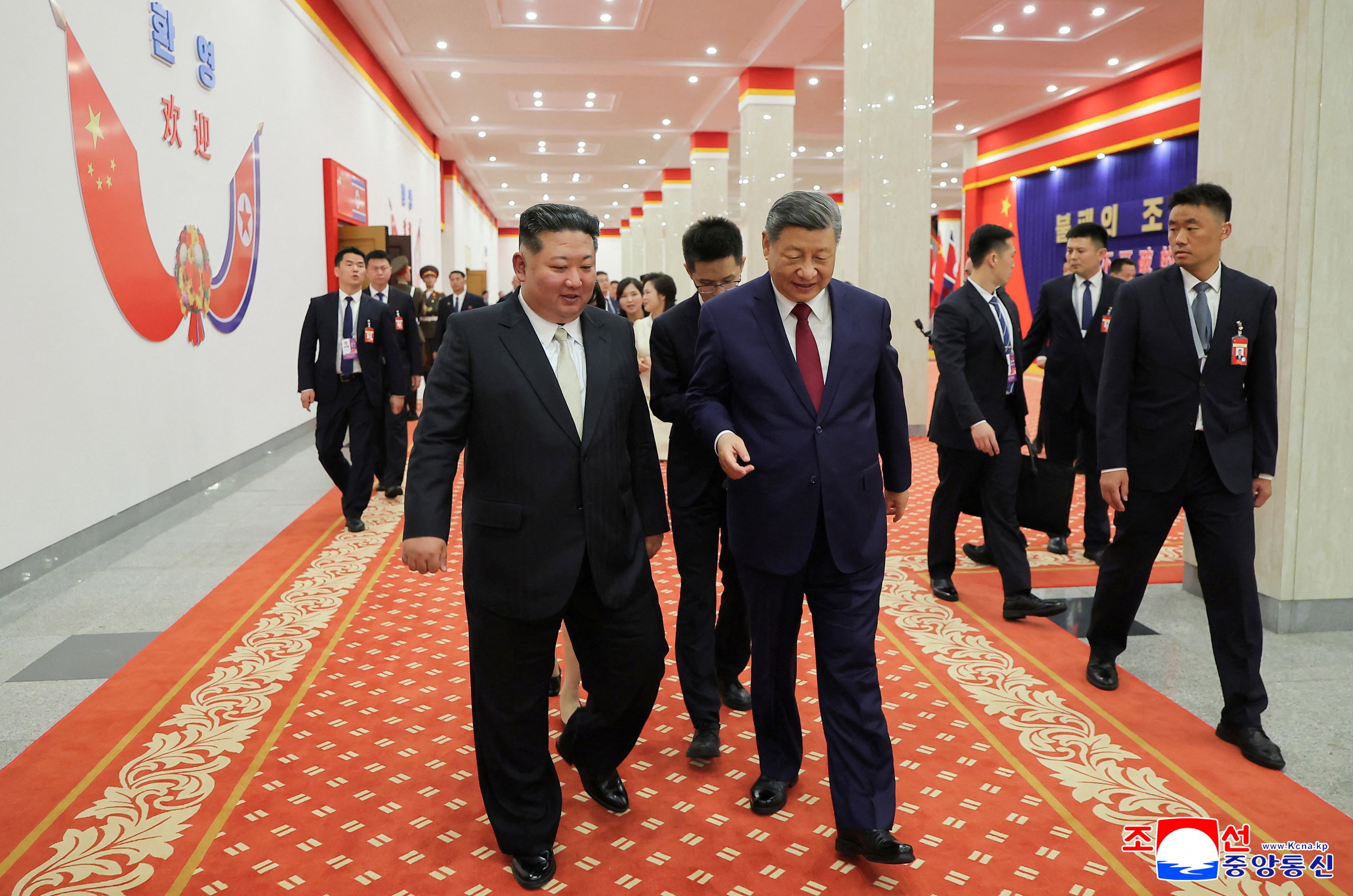 Xi Jinping and Kim Jong Un walk together along a decorated red carpet.