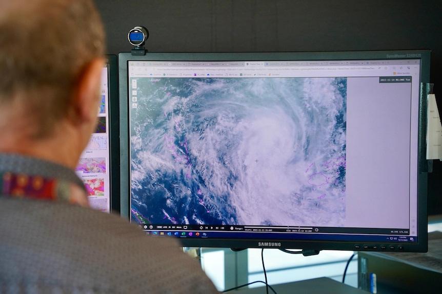 An over-the-shoulder look at a computer screen with cyclone imagery on it.