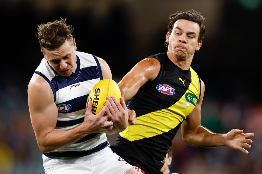 Mitch Duncan holds the ball as Daniel Rioli contests from beside him