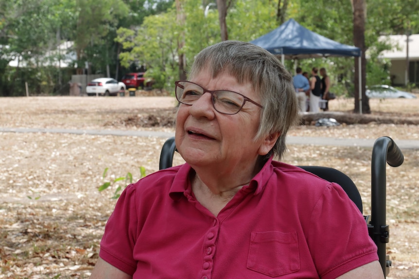 A woman wearing a red tshirt looks off camera. She is in a wheelchair.