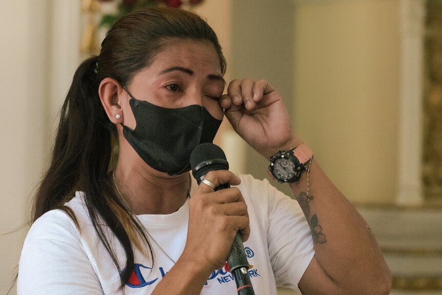 A woman in a black mask wipes a tear from her eye while holding a microphone 