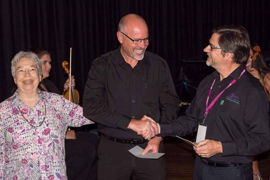 A woman and two men smiling handing over a cheque