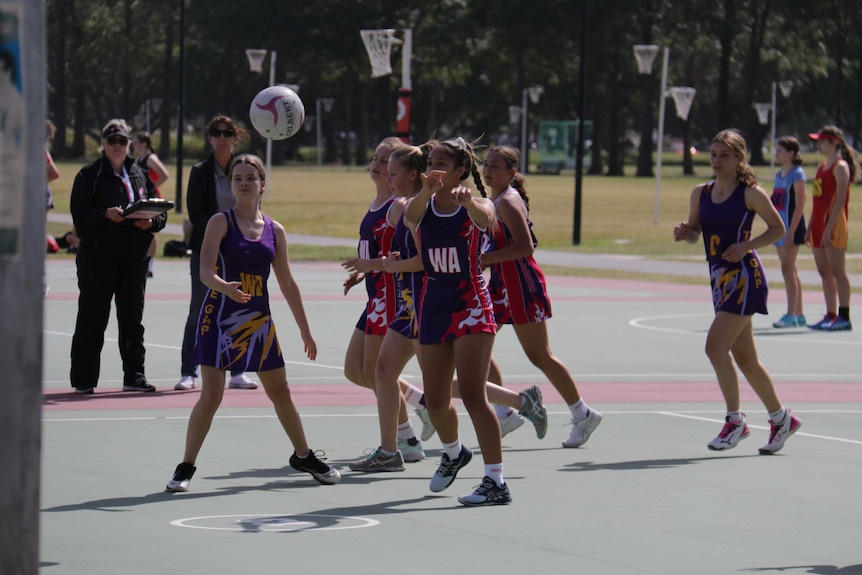 A girl wearing a red and blue netball uniform makes a pass during a netball game.
