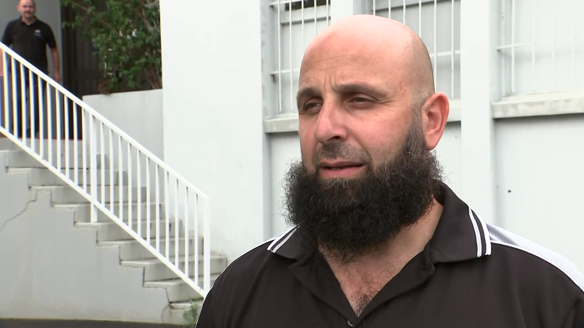 Man with beard stands in front of steps and wall