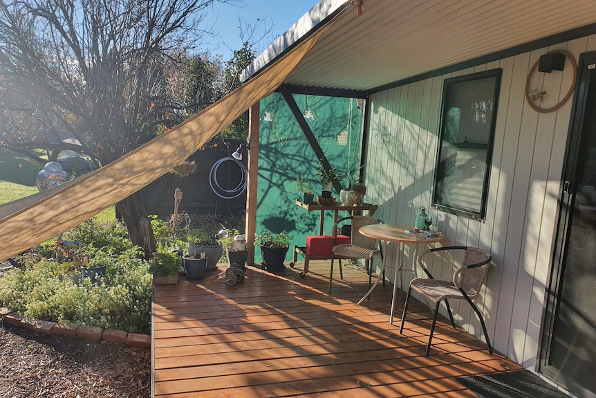 two chairs and a table sit on a covered deck with an outlook to a tree in the garden 