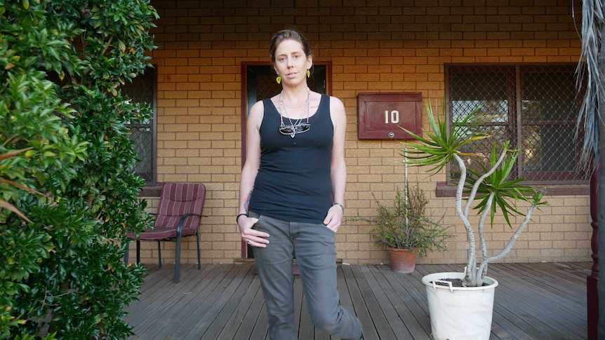 A woman stands in front of a brick house.