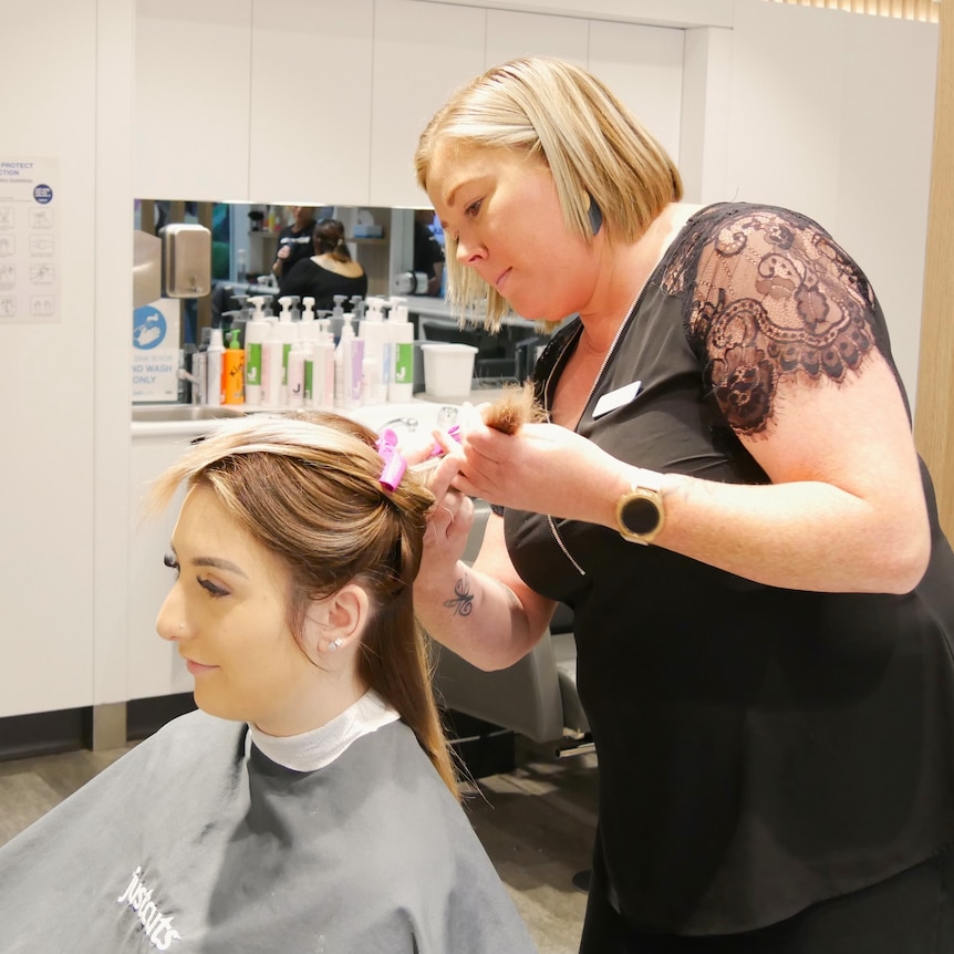 A woman wearing black cuts a womans hair. 