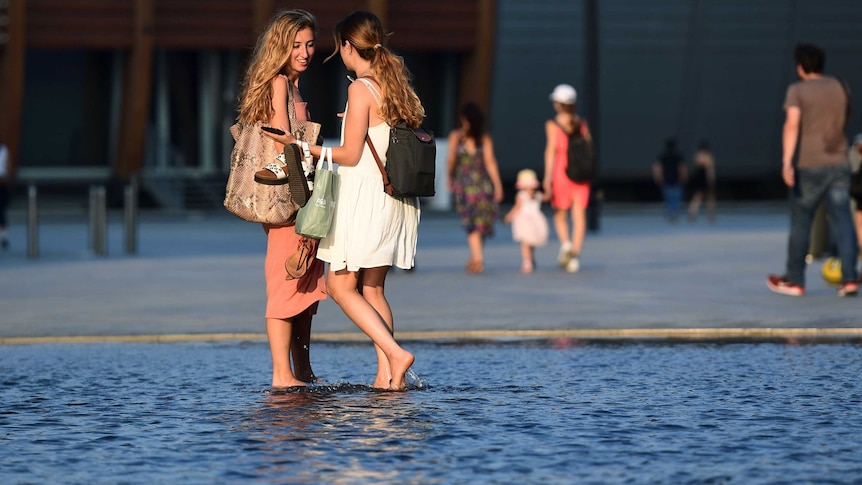 Women stand in a water fountain to cool down