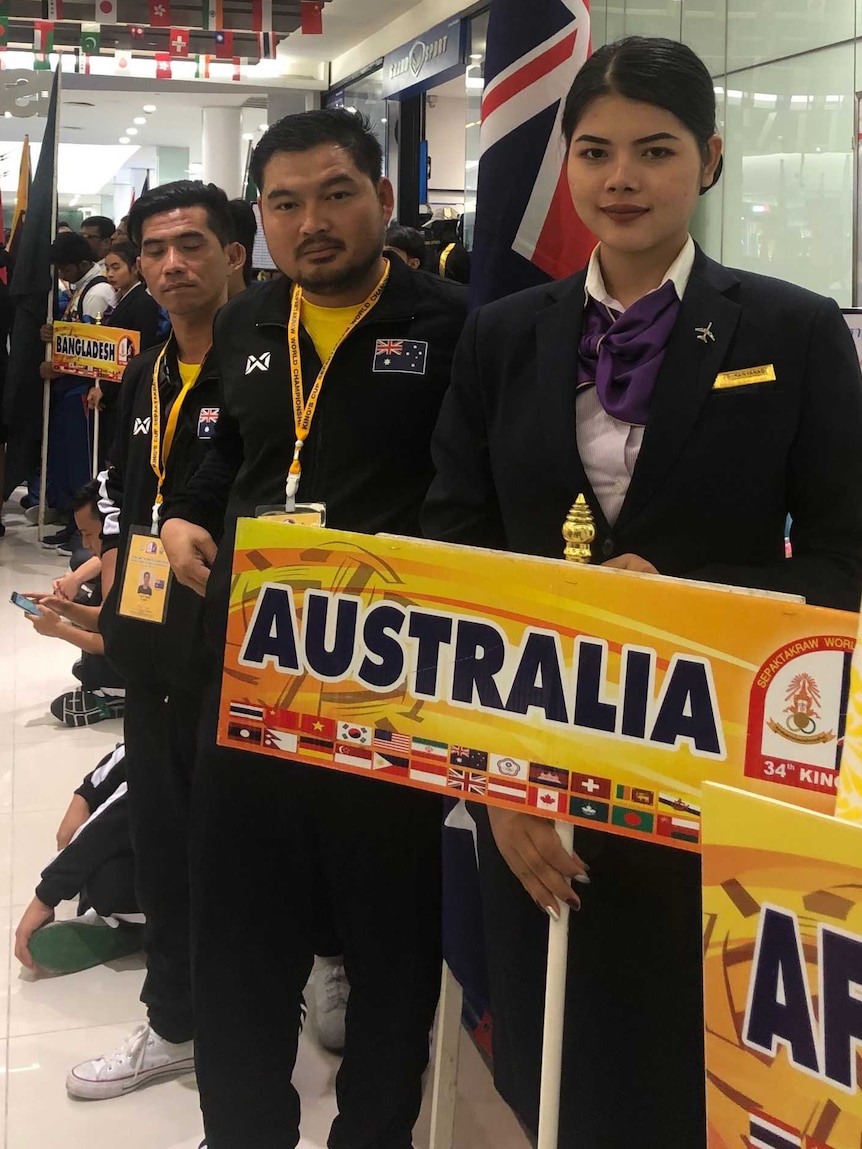 An East Asian man is wearing a sports uniform and holding a sign that says Australia.