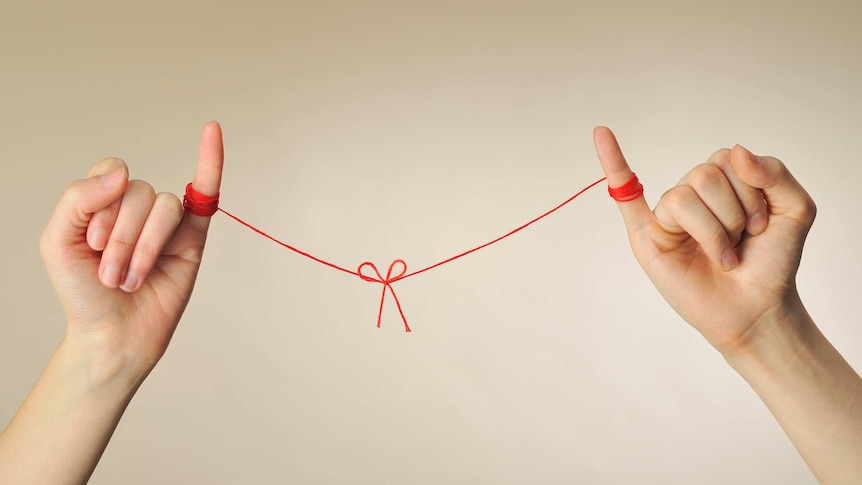 Stock photo of two hands with red string connecting the little finger of one hand to the other, to signify a 'pinky promise'.