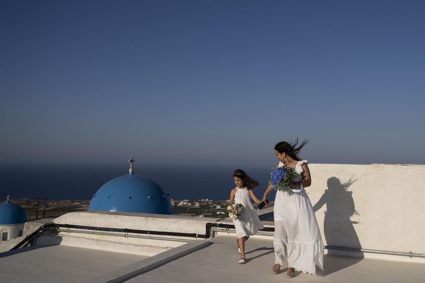 A mother and daughter hold hands as they walk on a rooftop 