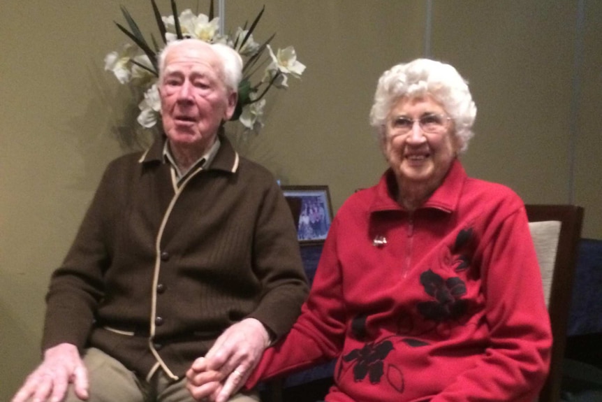 An elderly couple smiling and holding hands.