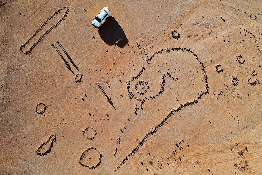 An aerial view of stone formations on a red-dirt landscape that dwarfs a four-wheel drive vehicle.