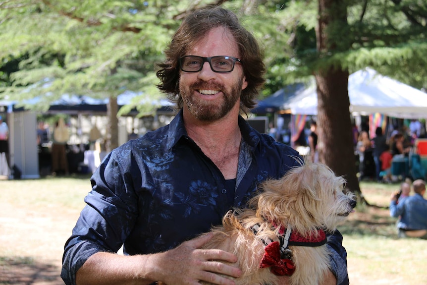 A man with a beard smiles at the camera, holding a fluffy dog.