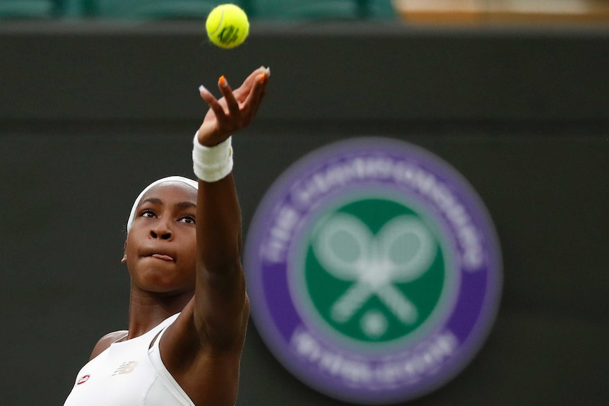 A girl with her arm outreached about to catch a tennis ball.