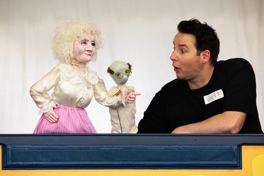 A man performs beside two puppets