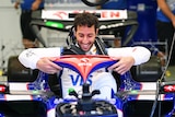 Male F1 driver Daniel Ricciardo lowers himself into his car, ready to race.