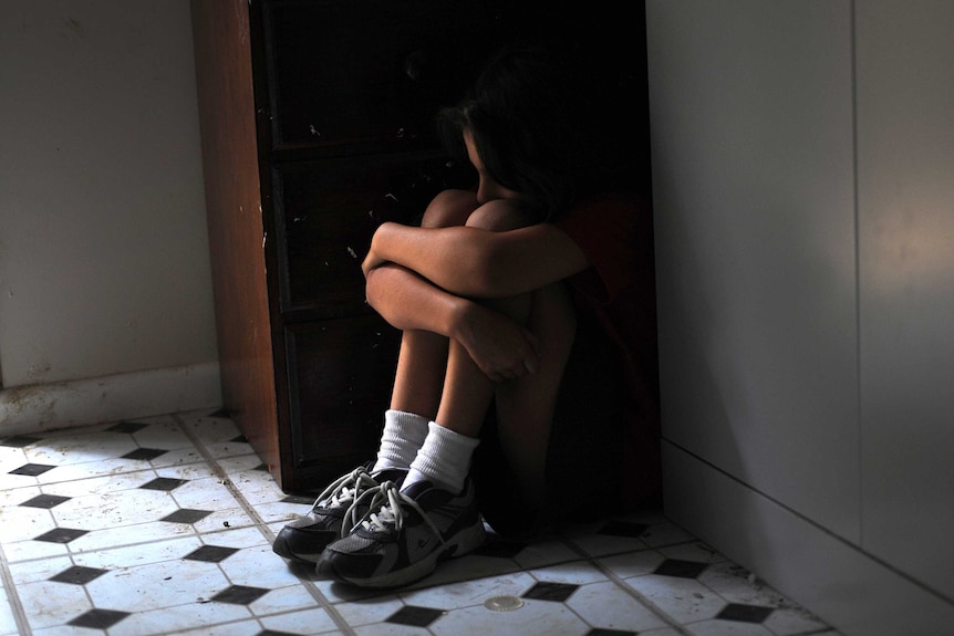 A girl shields herself in the corner of a room