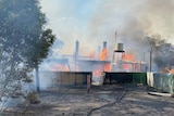 A photo of a homestead on fire with a nearby water tank and trees.
