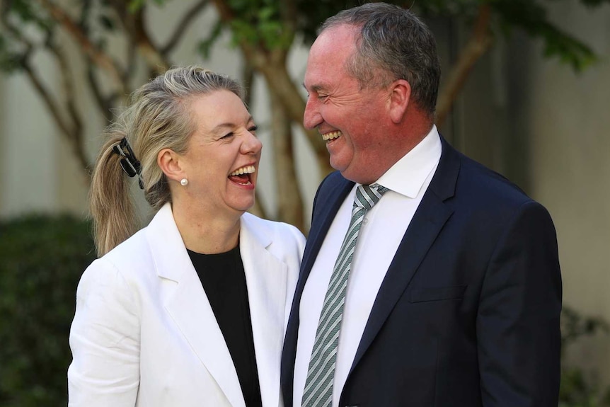 A woman and man standing in a courtyard looking at each other laughing