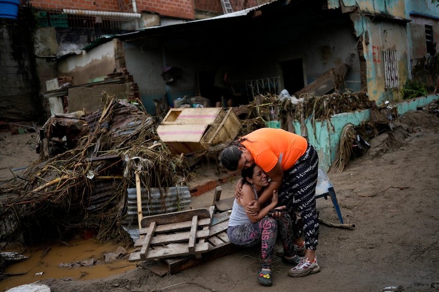 A woman is comforted as she cries in front of a damaged house. 