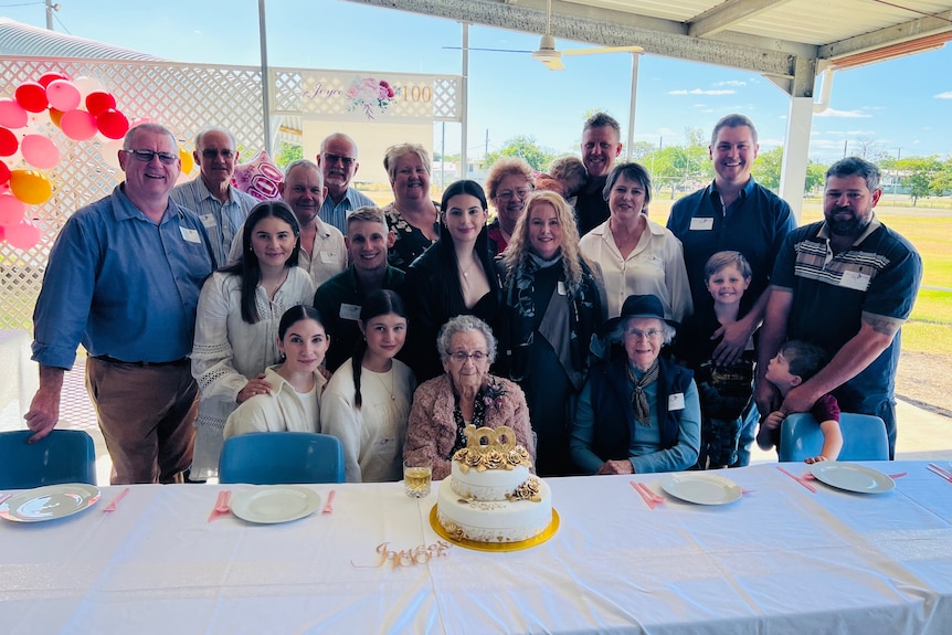 An elderly woman with a birthday cake surrounded by people.