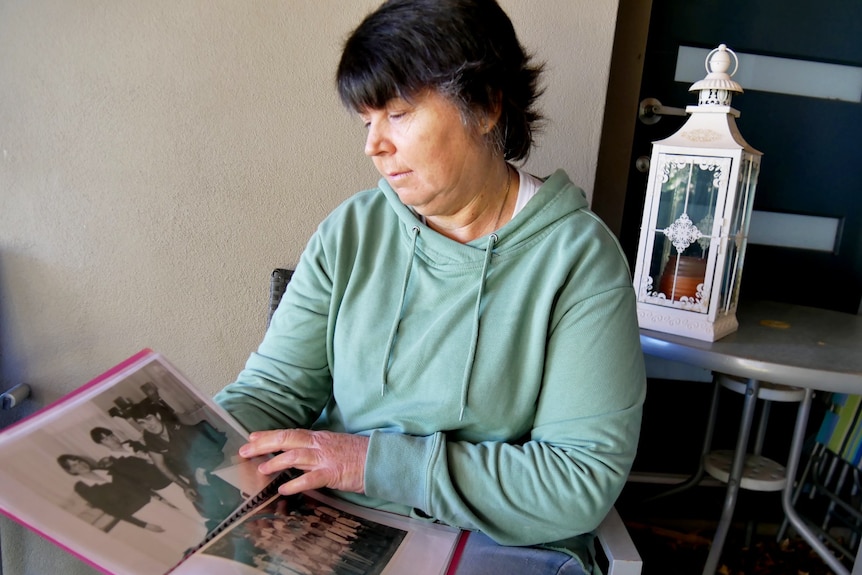 A woman in a green jumper sitting down looking at old photos in a folder.
