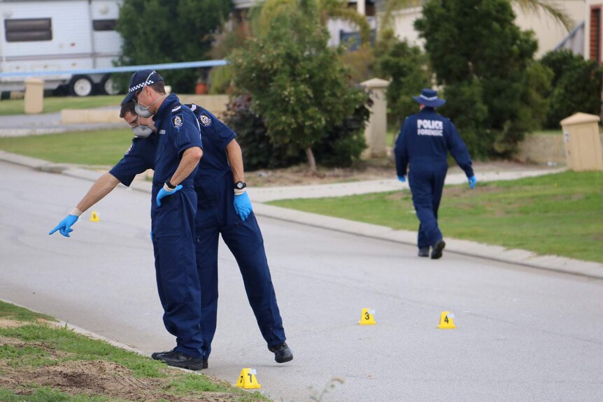 Two forensics officers in blue suits look at something on the ground in a Banksia Grove Street.