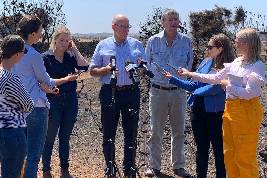 Two older men speak to a group of female reporters