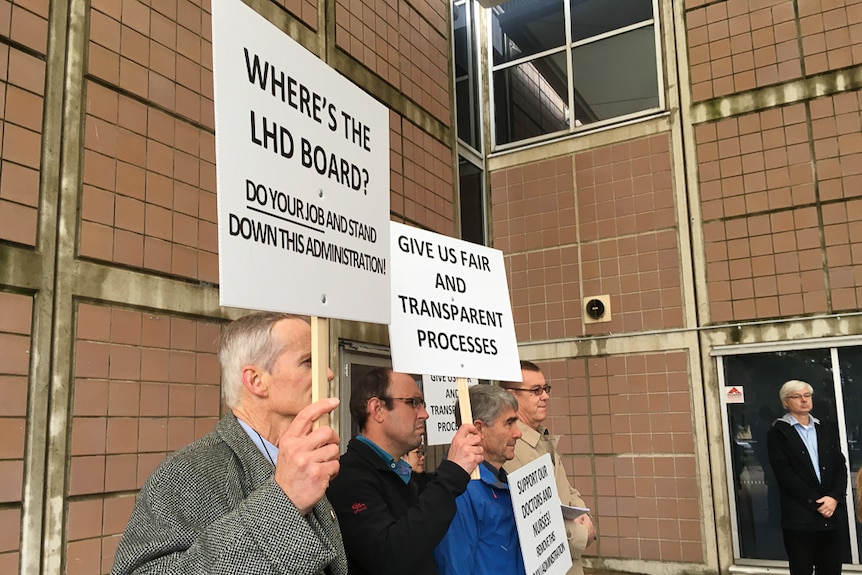 Side view of men standing holding signs saying Where's the LHD Board, give us fair and transparent process