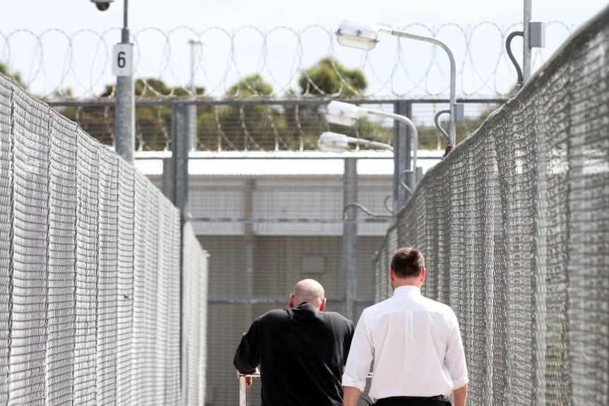 Two men walking along walkway in prison