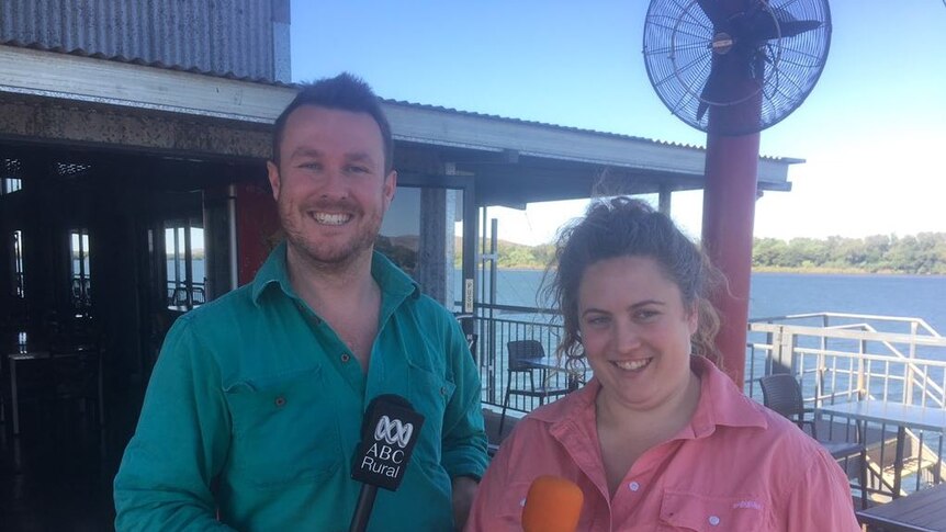 a man in a green shirt and a woman in a pink shirt with a lake behind.