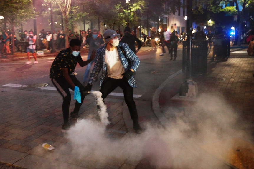 A man holds a smoke bomb amid a crowd of protesters at night