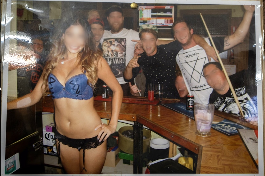 A woman in her underwear poses in a pub with men looking on.