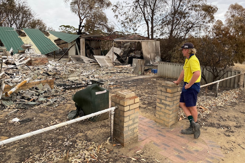 a boy looks at a destroyed home with an asbestos fence