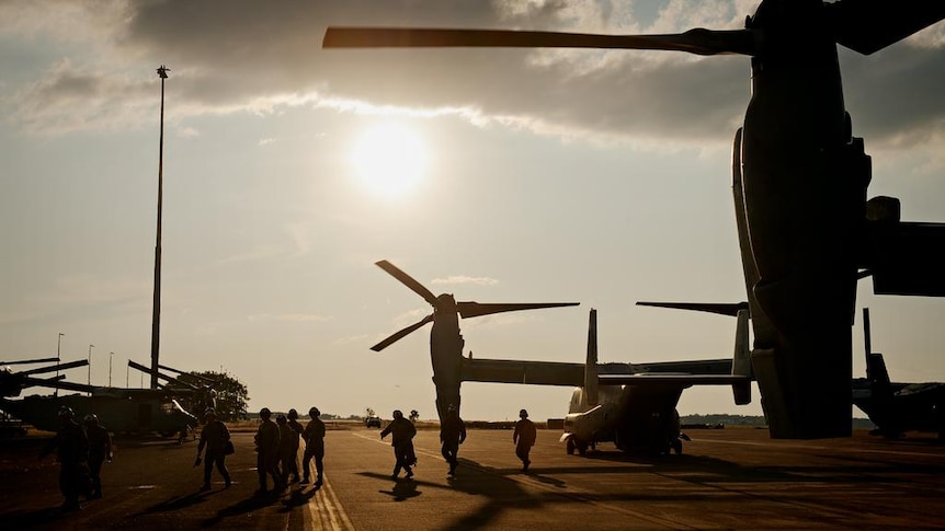 A handful of soldiers next to a large military aircraft, on a tarmac, silhouetted against the sun