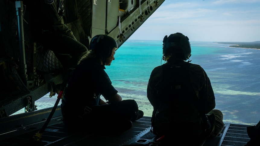 Two uniformed individuals overlooking ocean in New Caledonia from military plane