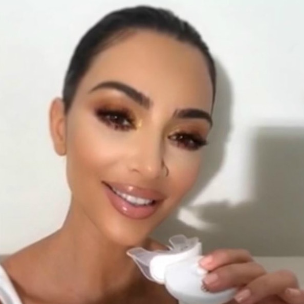 A Kardashian uses a teeth-whitening mouthguard while applying make-up.
